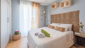A neatly made bed with pillows and a blanket, a bedside table with a vase, a wooden headboard, and a ceiling fan. - Modern and only a few steps from the sea - Apartamento Soñac S (Los caños de meca ( Cadiz))