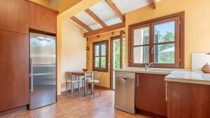 Eine Küche mit Holzausstattung, einem Edelstahlkühlschrank, einem Geschirrspüler und einem Fenster mit Blick ins Grüne.