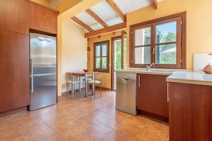 A kitchen with wooden cabinets, a stainless steel refrigerator, a dishwasher, and a window with a view of greenery.