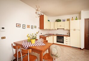 Une cuisine compacte avec des meubles en bois, une table à manger avec des chaises et un petit îlot central agrémenté d’un vase de fleurs.