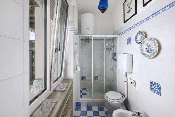 A bathroom with a glass shower enclosure, a toilet, and a sink.