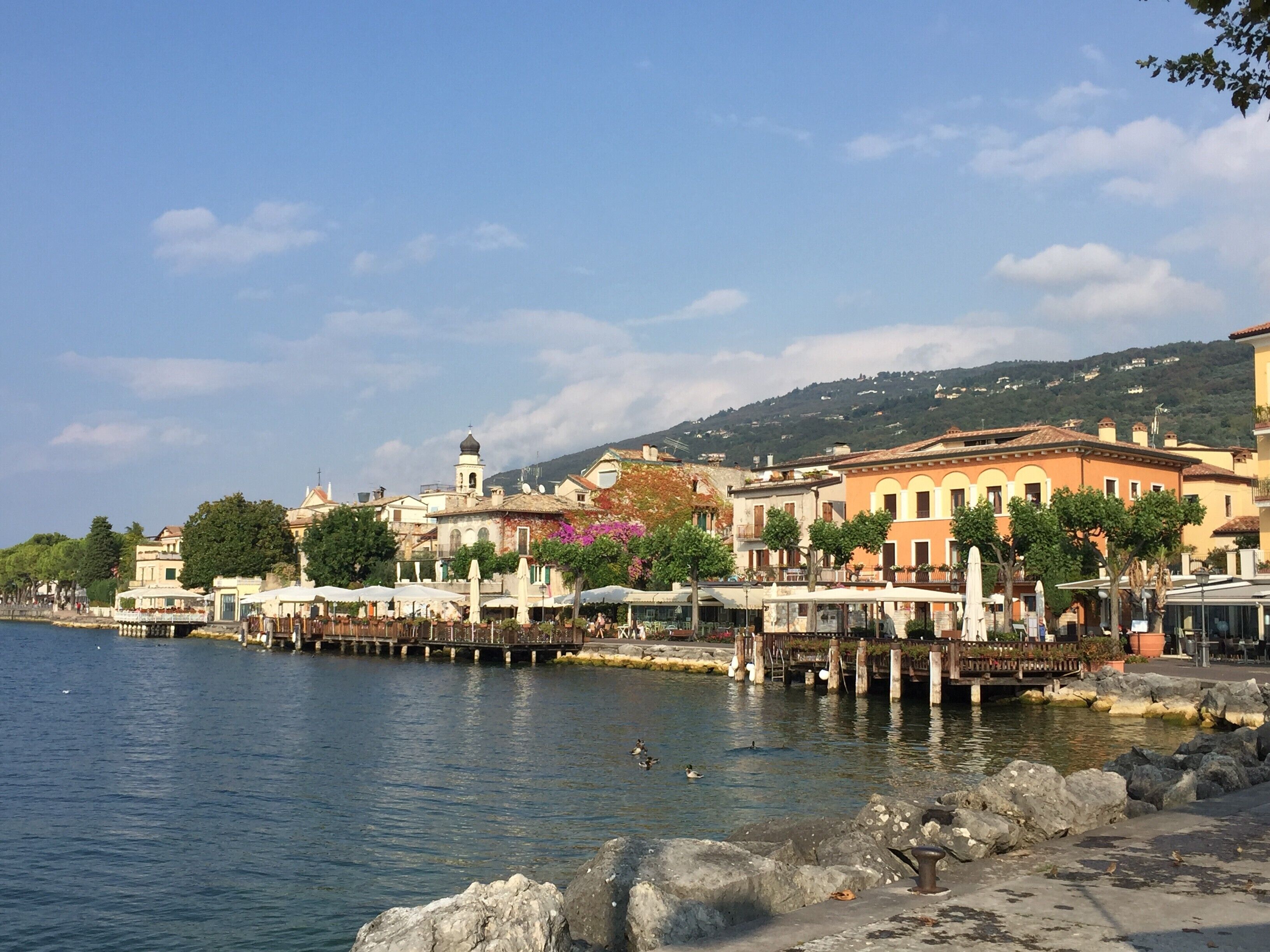 Una zona costera con edificios, un muelle y una colina al fondo.