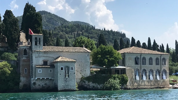 A historic building with a bell tower, a statue, and a view of the water.