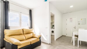 A modern living room with a sofa, a dining table, and a kitchen area visible through an open door. - Modern, with roof terrace and very close to the beach - Apartamento La Perla (Conil de la Frontera)