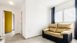 A room with a sofa, a window with curtains, a door leading to another room, and a light switch on the wall. - Modern, with roof terrace and very close to the beach - Apartamento La Perla (Conil de la Frontera)