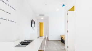 A modern, minimalist room with a white desk, a flat-screen TV mounted on the wall, and a yellow accent wall in the background. - Modern, with roof terrace and very close to the beach - Apartamento La Perla (Conil de la Frontera)