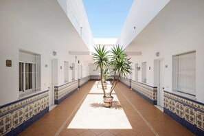 Un couloir aux murs blancs, au sol carrelé et agrémenté de plantes en pot.