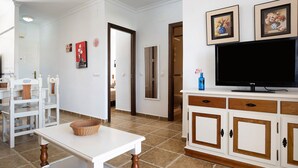 Un soggiorno con televisore, mobili bianchi e pavimento piastrellato.