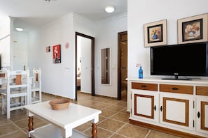 A living room with a television, white furniture, and a tiled floor.
