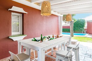 A covered patio with a white table and chairs, a hanging lantern, and a pool in the background.