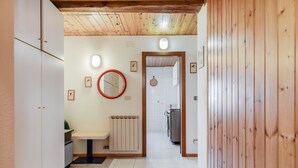 A hallway with a wooden ceiling, a white radiator, a round mirror, and a door leading to a kitchen area. - Apartment “Mansarda tra le Dolomiti di Brenta" with Mountain View & Balcony (Bocenago)