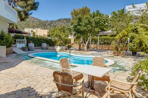 A pool area with wicker furniture, stone flooring, and surrounding greenery. - Fantastic holiday Apartment La Cabanya 3B, Shared Pool, Terrace & Wi-Fi (CANYAMEL)