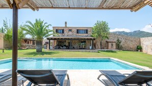 A poolside area with lounge chairs, a stone building with a patio, and a clear view of the pool.
