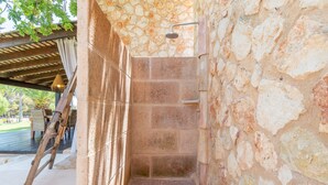 A stone-walled shower area with a tiled floor, a wooden ladder, and a metal showerhead.