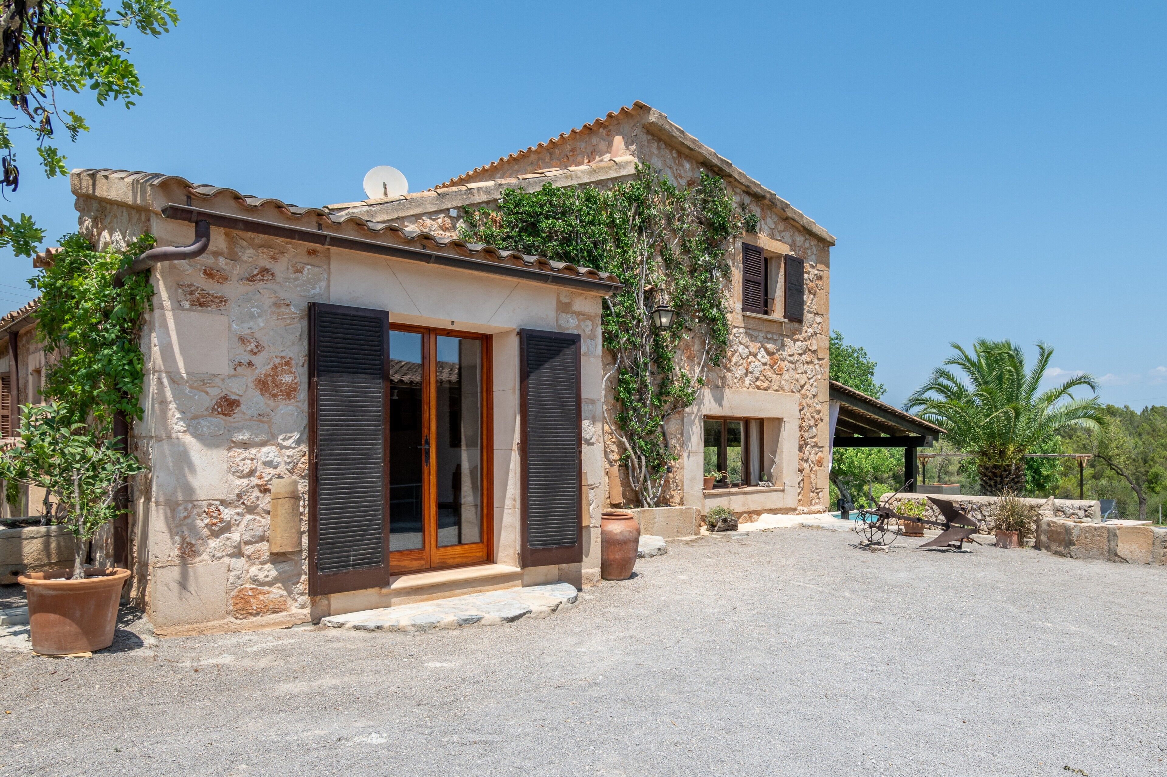 A stone house with a tiled roof, large windows, and potted plants.