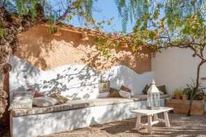 A cozy outdoor seating area with a cushioned bench, a lantern, and potted plants. - Beautiful Country Home with 2 Pools, Wi-Fi, Air Conditioning (Santanyí)