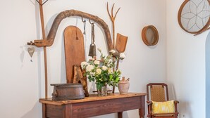 Un interior rústico con una mesa de madera, una silla, un florero con flores y varios objetos de madera en la pared.