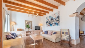 Una sala de estar con sofá, sillón, mesa de centro, televisor y una obra de arte en la pared.