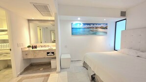 Een moderne slaapkamer met een groot bed, een badkamer met een wastafel en uitzicht op het strand.
