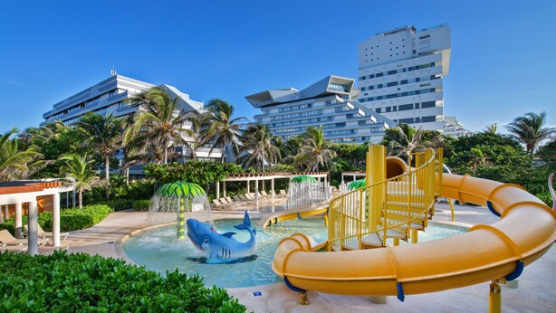 Een waterpark met een glijbaan, een zwembad met een haai-rubber en palmbomen.