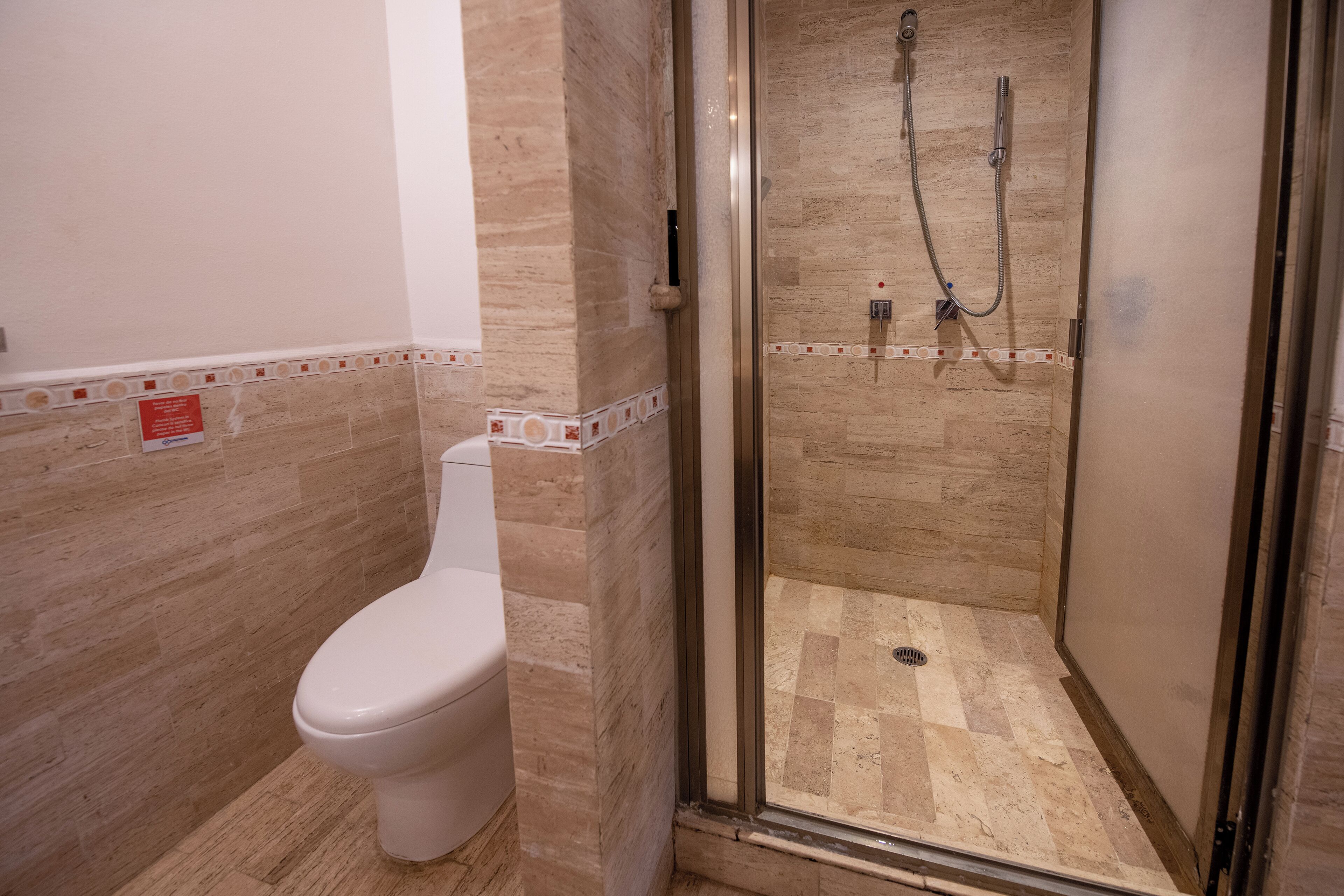 Un baño con inodoro, ducha con puerta de cristal y suelo de baldosas.