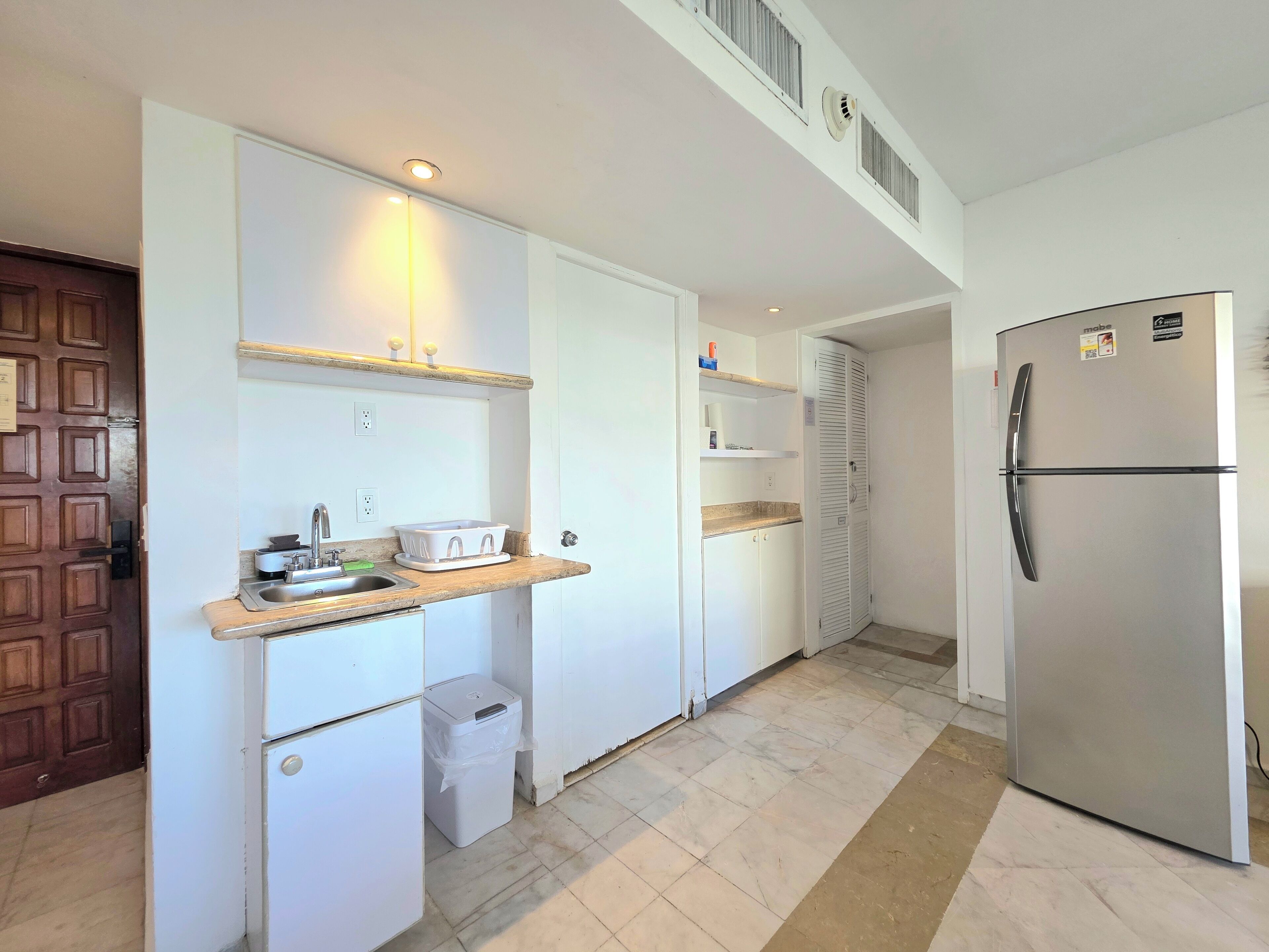 A compact kitchen with white cabinetry, a stainless steel refrigerator, and a small countertop with a sink.