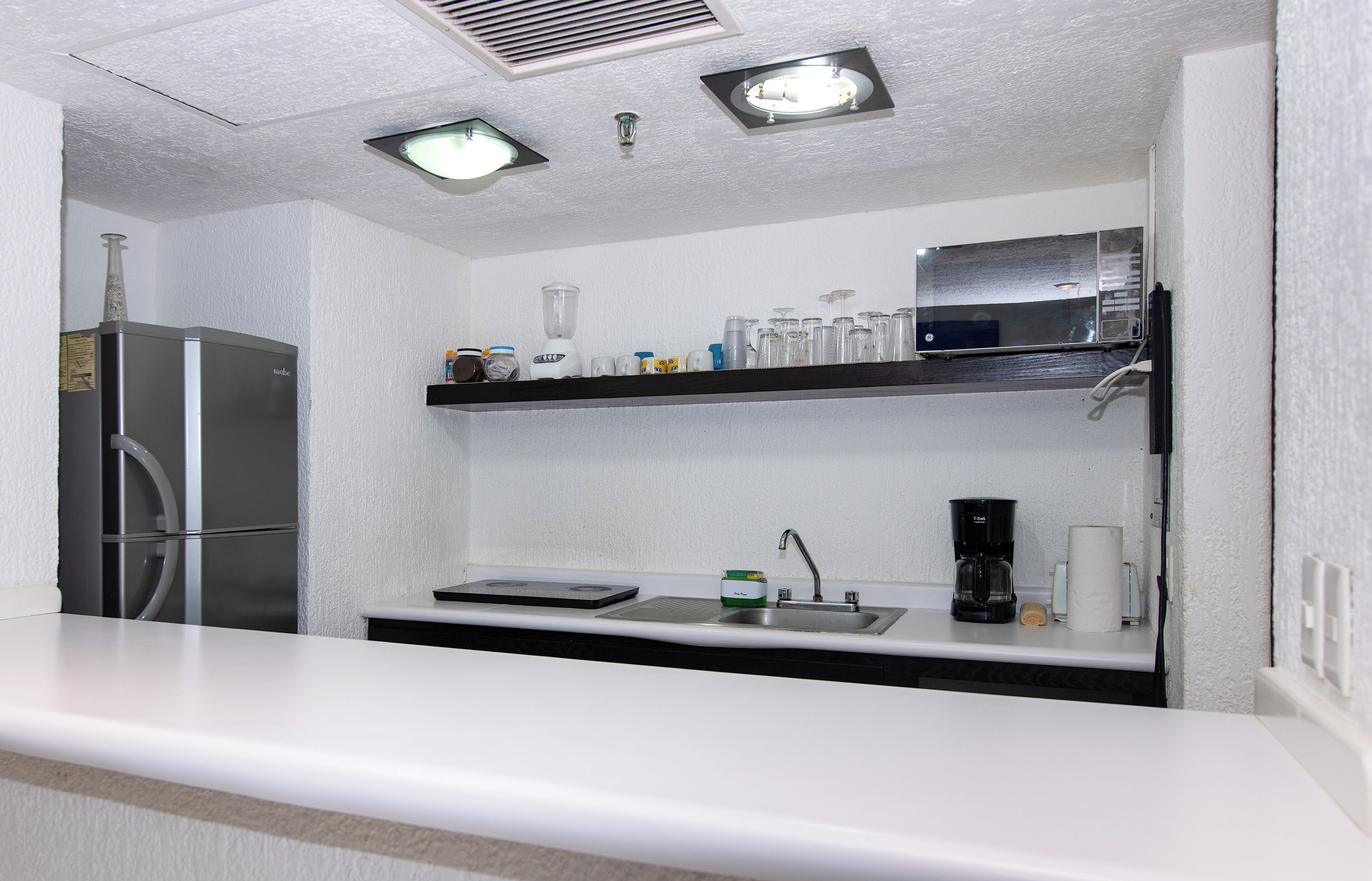 A compact kitchenette with a stainless steel refrigerator, a microwave, a coffee maker, and a sink.