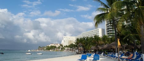 A beach with white sand, palm trees, and a hotel in the background.