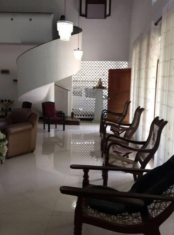 Relax in this stylish living area with a high ceiling, featuring a comfortable sofa, a wooden chair, and a potted plant.