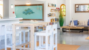 Un salon moderne avec une table à manger en bois, des chaises blanches, une bibliothèque, un canapé et une grande fenêtre.