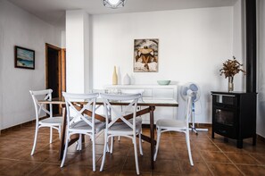 A dining area with a white table and chairs, a black stove, and a painting on the wall.