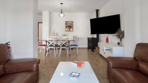 A living room with a TV, leather sofas, a coffee table, and a dining area with chairs and a table.