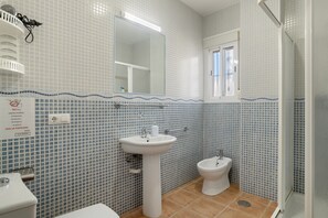 Een badkamer met een wastafel, toilet en bidet, betegelde wanden, een spiegel en een raam.