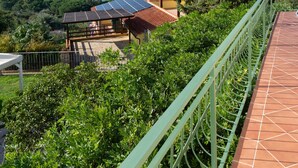 A terrace with a view of the sea, surrounded by greenery and a metal railing.