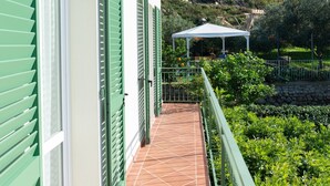 A balcony with green shutters, a tiled floor, and a white building with a garden view.