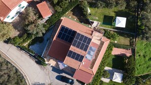 An aerial view of a house with a red roof, solar panels, a swimming pool, and a car parked in the driveway.