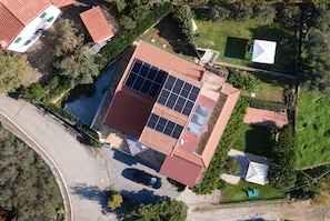 Une vue aérienne d’une maison avec un toit rouge, des panneaux solaires, une piscine et une voiture garée dans l’allée.