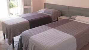 A hotel room with two beds, a sliding glass door, a wall-mounted lamp, and a view of the outdoors.