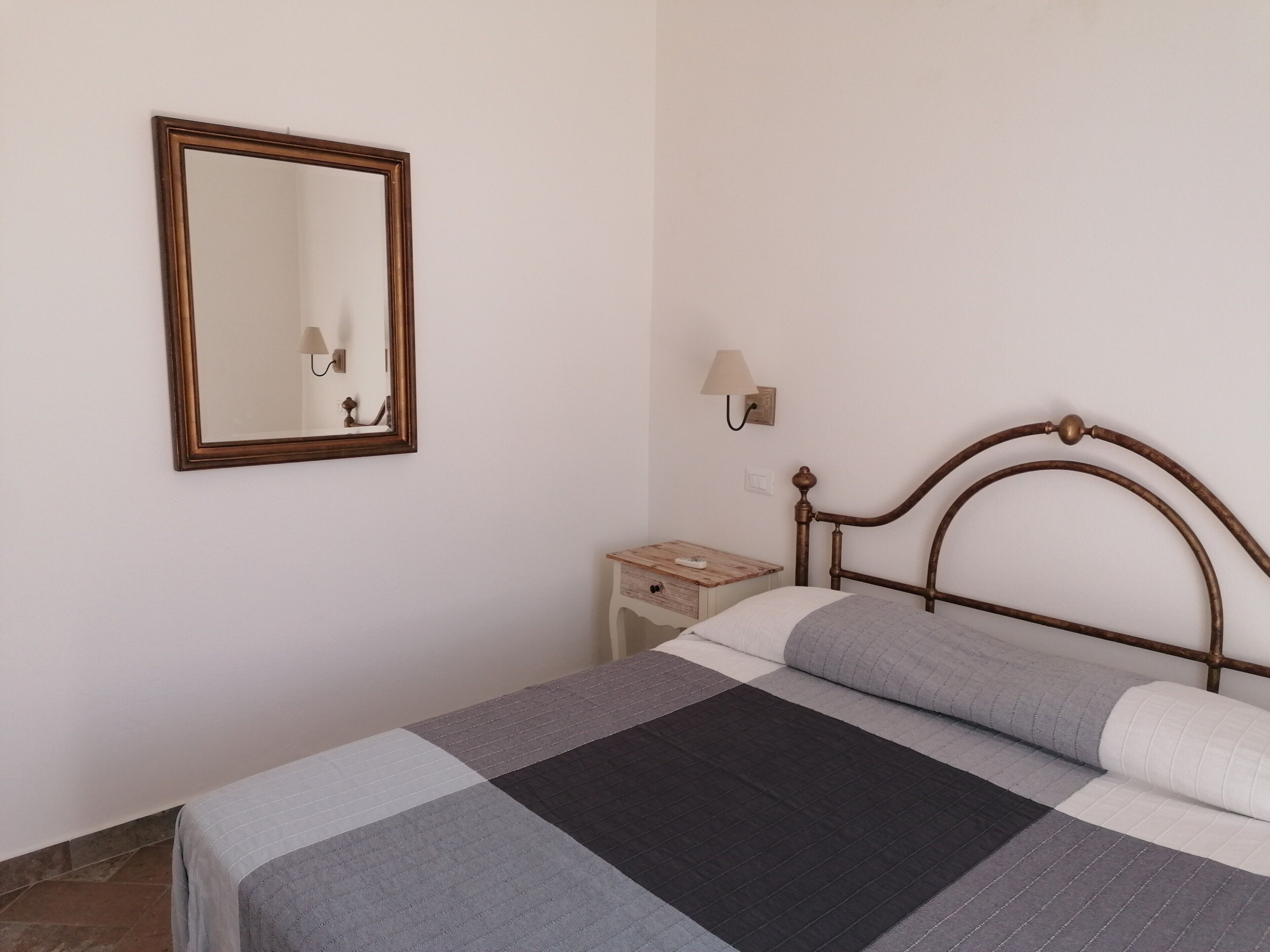 A bedroom with a bed, a nightstand, a wall-mounted lamp, and a mirror.