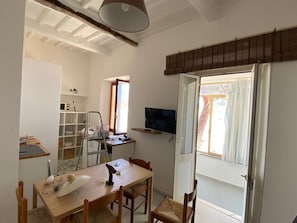 A compact kitchen with a dining table, chairs, a TV mounted on the wall, and a sliding glass door leading to an outdoor area.