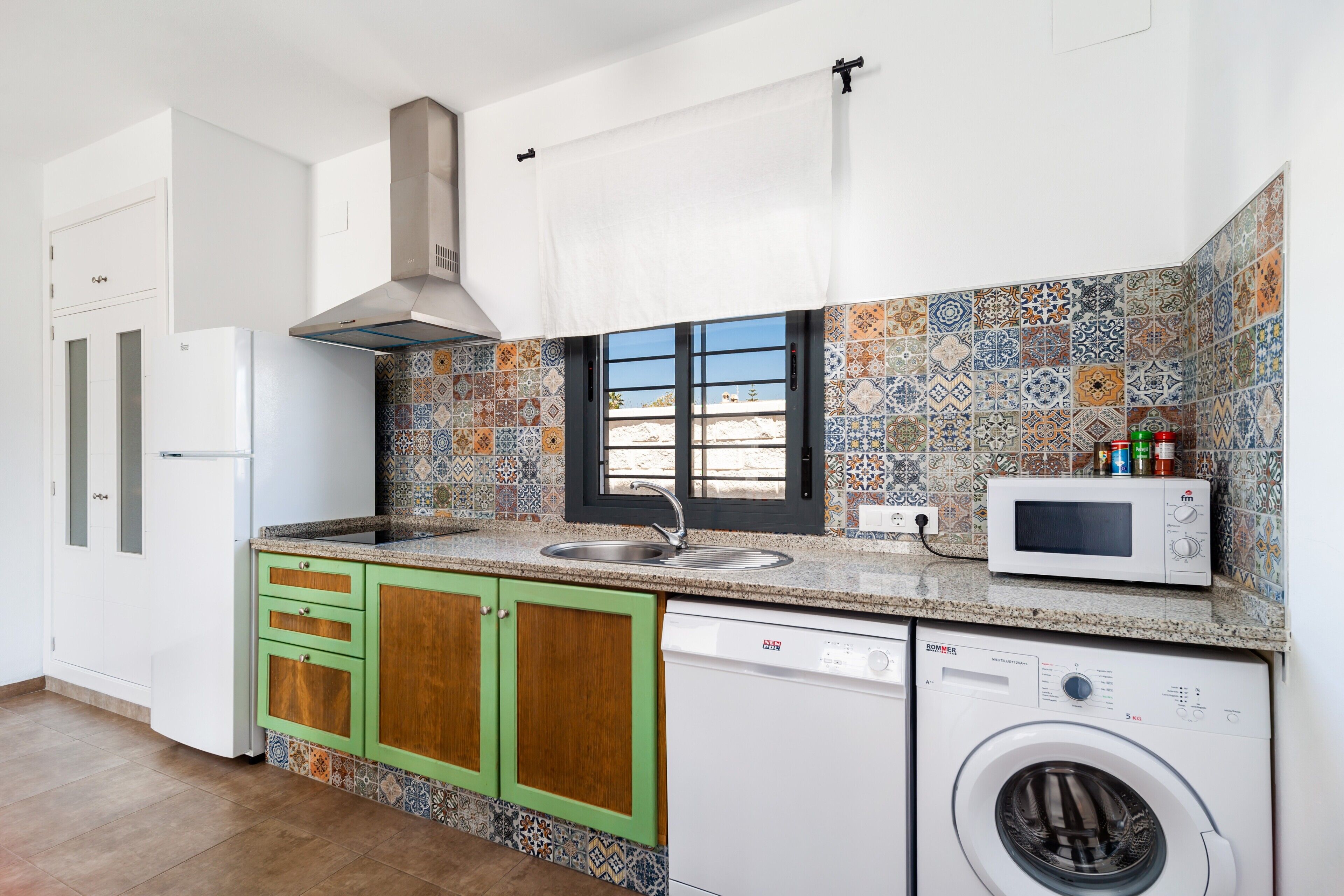 A kitchen with a washing machine, a microwave, and a window with a view.