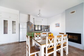 A modern kitchen with white cabinets, a dining table with wooden chairs, a microwave, and a black fireplace.