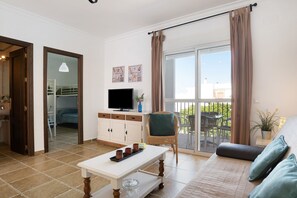 A living room with a sofa, a coffee table, a television, and a balcony with a view.