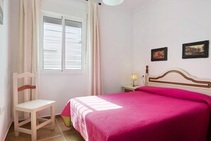 A bedroom with a bed, a chair, a nightstand, a lamp, and two framed pictures on the wall.