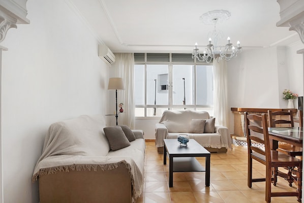 A living room with a sofa, armchair, dining table, and chandelier.