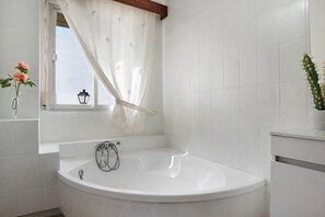 Een moderne badkamer met een vrijstaand bad, een raam met gordijn, en een cactus.