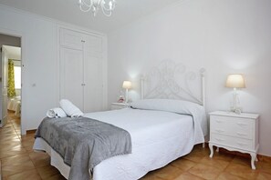 Een slaapkamer met een bed, witte nachtkastjes, een kapstok en een kroonluchter.