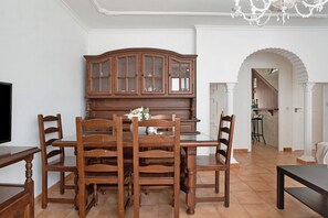 A dining area with a wooden table and chairs, a cabinet with glass doors, and a chandelier.