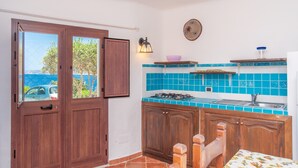 A kitchen with wooden cabinets, a gas stove, a sink, and a view of the sea through a door.