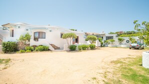 A white villa with a paved driveway, a stone wall, and a car parked in the background.